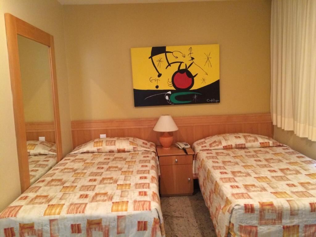 Habitación de hotel con dos camas, una mesita de noche con lámpara, teléfono y un cuadro en la pared.