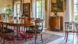 Una sala da pranzo con un tavolo rotondo in legno, diverse sedie, un quadro di grandi dimensioni e una finestra con tende.