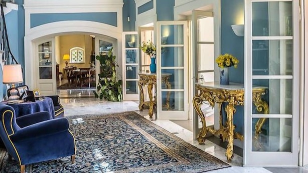 Spaziosa hall con colori blu e bianco, caratterizzata da una maestosa scala, arredi eleganti e un'ampia finestra che offre vista sull'interno.