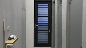 A narrow hallway with a tiled floor, a black-framed door with horizontal slats, and a small shelf with a white object on the left. - Welcome Hostel (Hualien City)