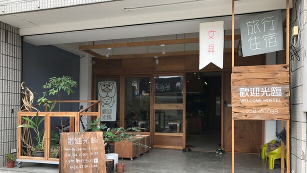 A hostel entrance with a wooden facade, a welcome sign, and a signboard with operating hours. - Welcome Hostel (Hualien City)