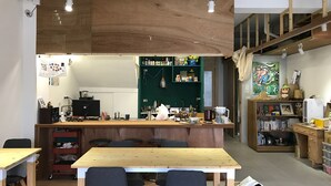 A modern, open-plan living space with a central wooden table, multiple seating options, and a kitchen area visible through a green partition. - Welcome Hostel (Hualien City)