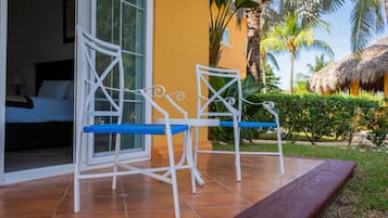 Un patio con dos sillas de metal blanco con cojines azules, una cama con ropa de cama blanca y una pared amarilla.