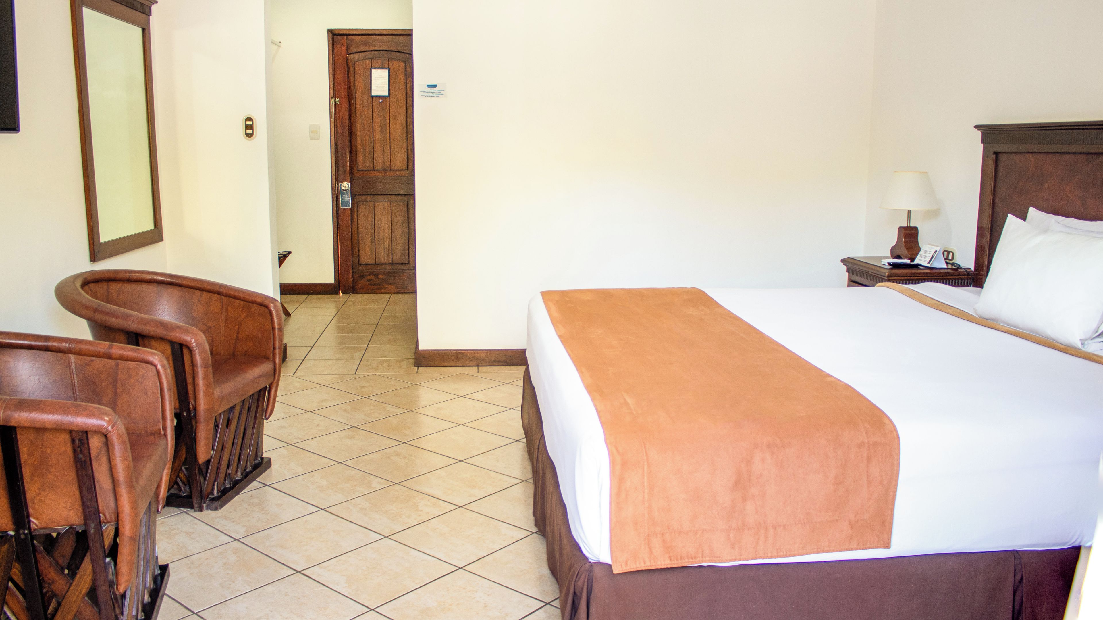 Une chambre d’hôtel avec un lit, une table de chevet, une lampe, une chaise et une porte.