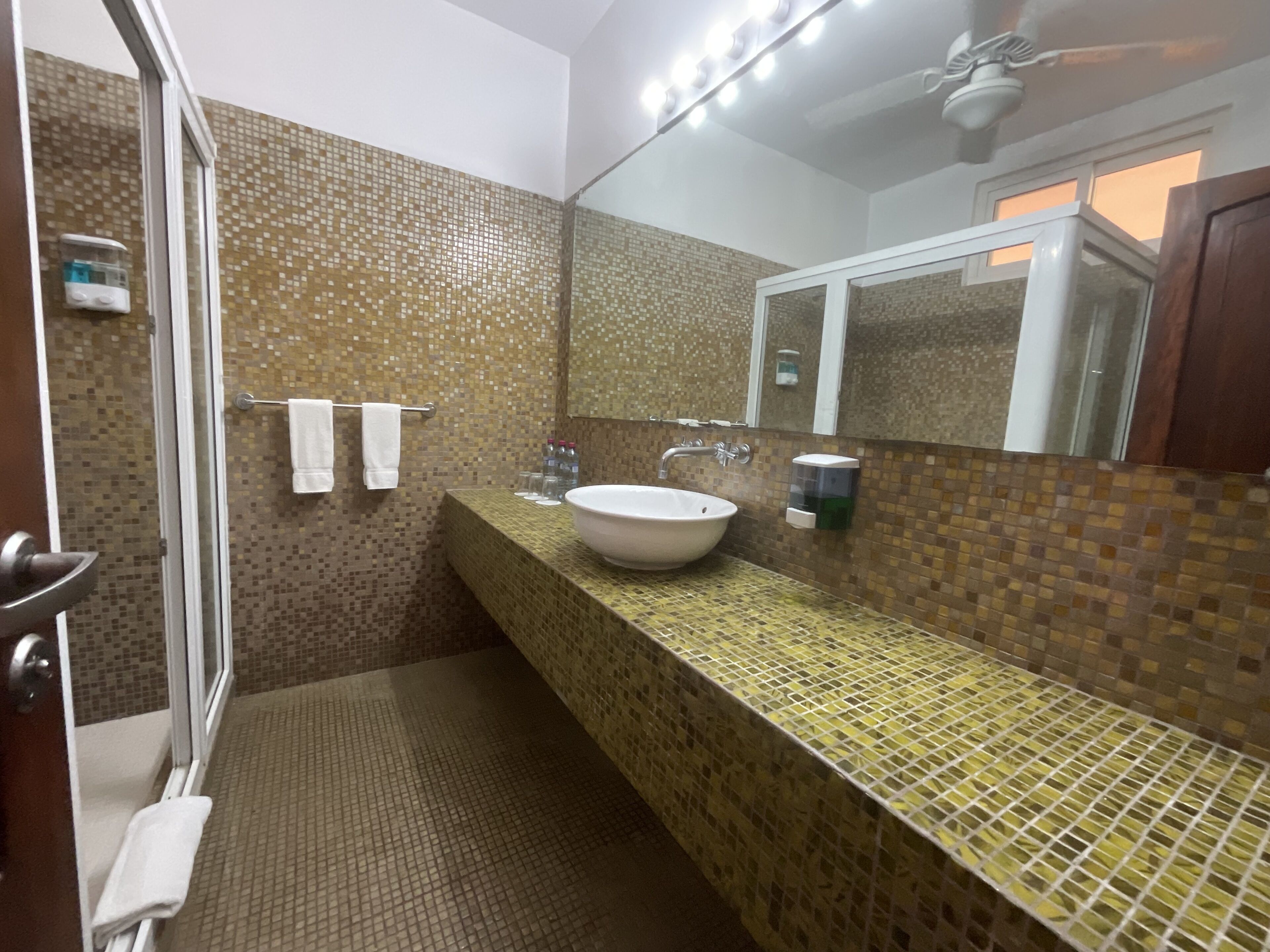 Un baño con pared de mosaicos, un espejo grande, un lavabo y una zona de ducha.