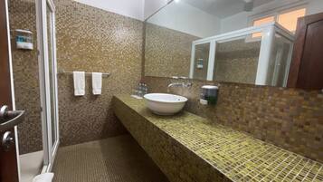 Un baño con pared de mosaicos, un espejo grande, un lavabo y una zona de ducha.