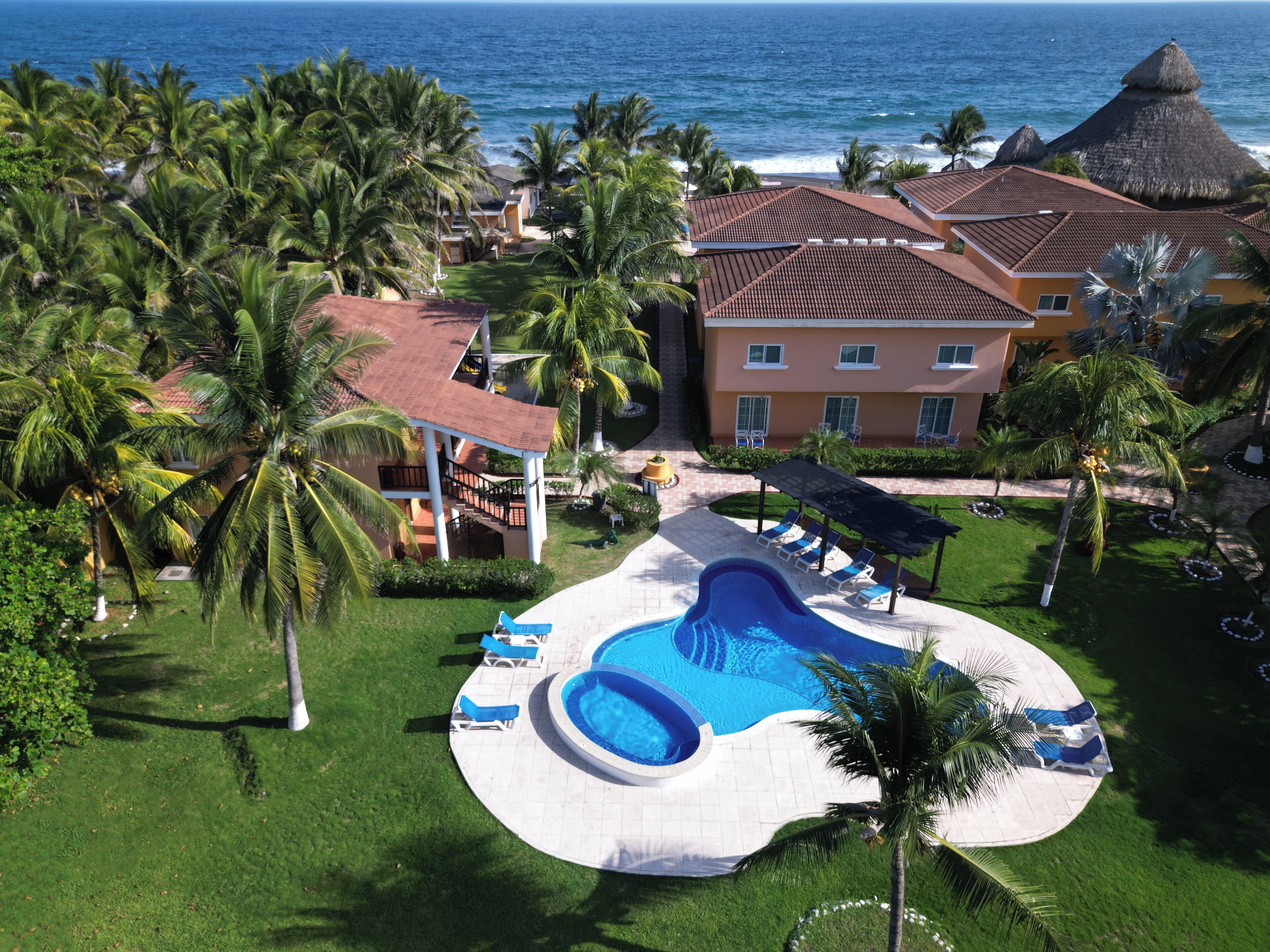 Un resort con piscina, palme e vista sull'oceano.