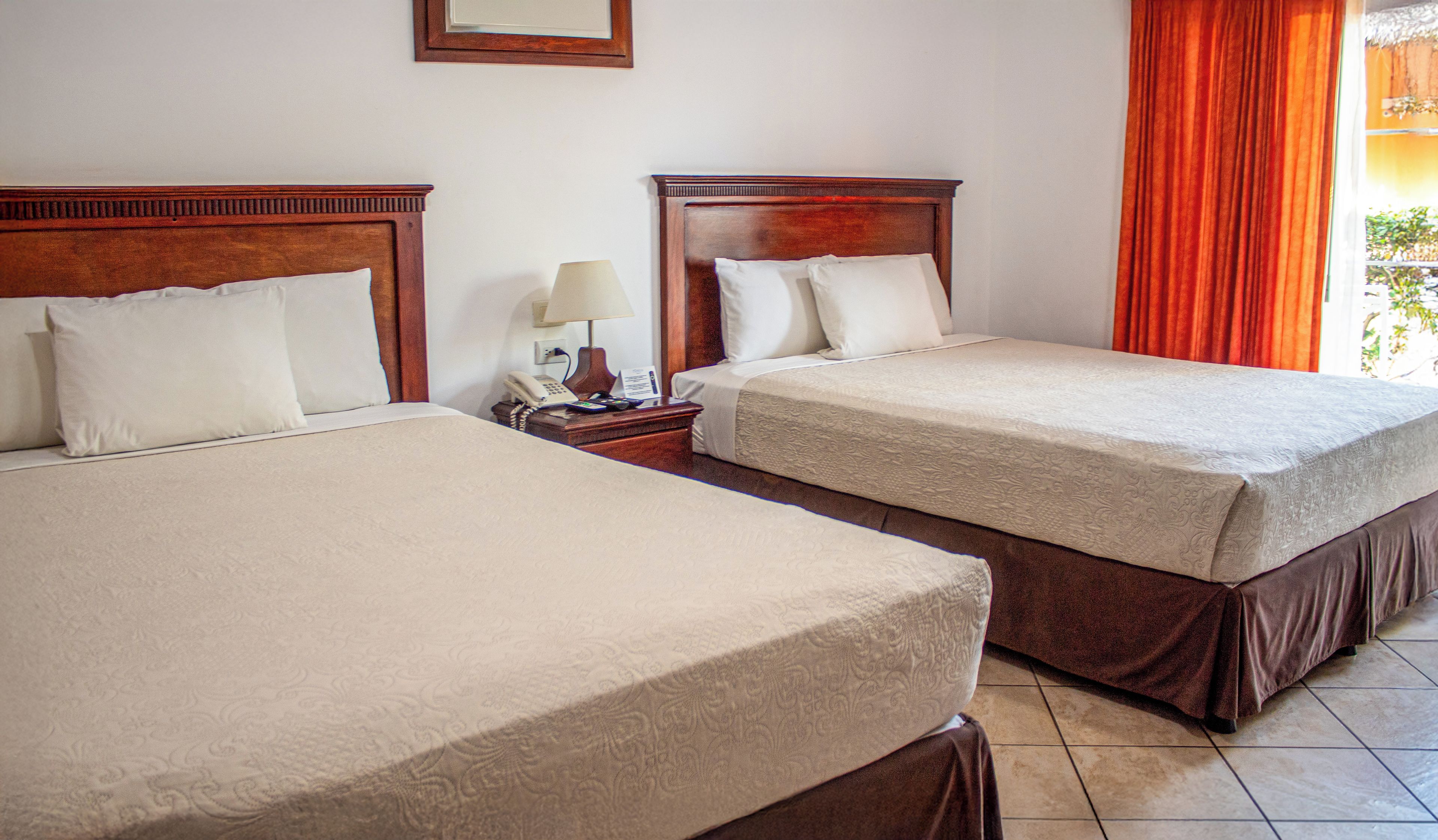 A hotel room with two beds, each with a wooden headboard, a bedside table with a lamp, and a telephone.