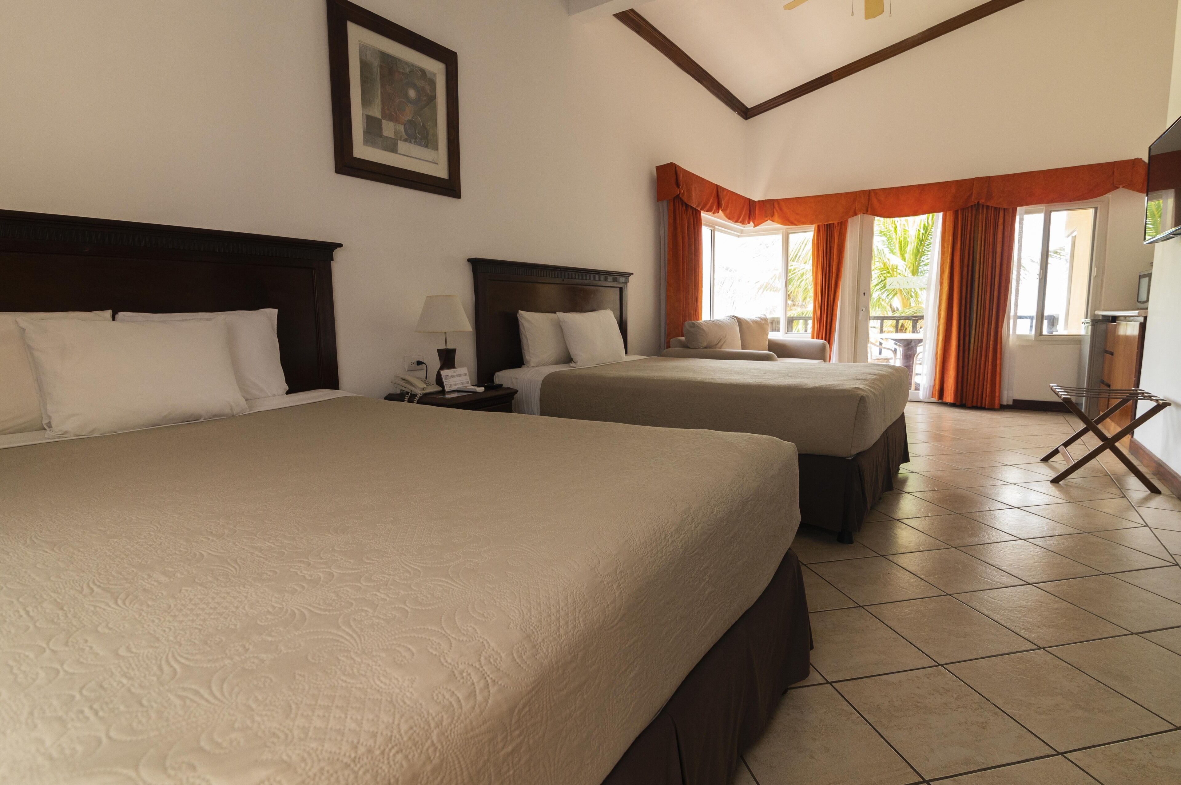 A hotel room with two beds, a TV, and a balcony with orange curtains.