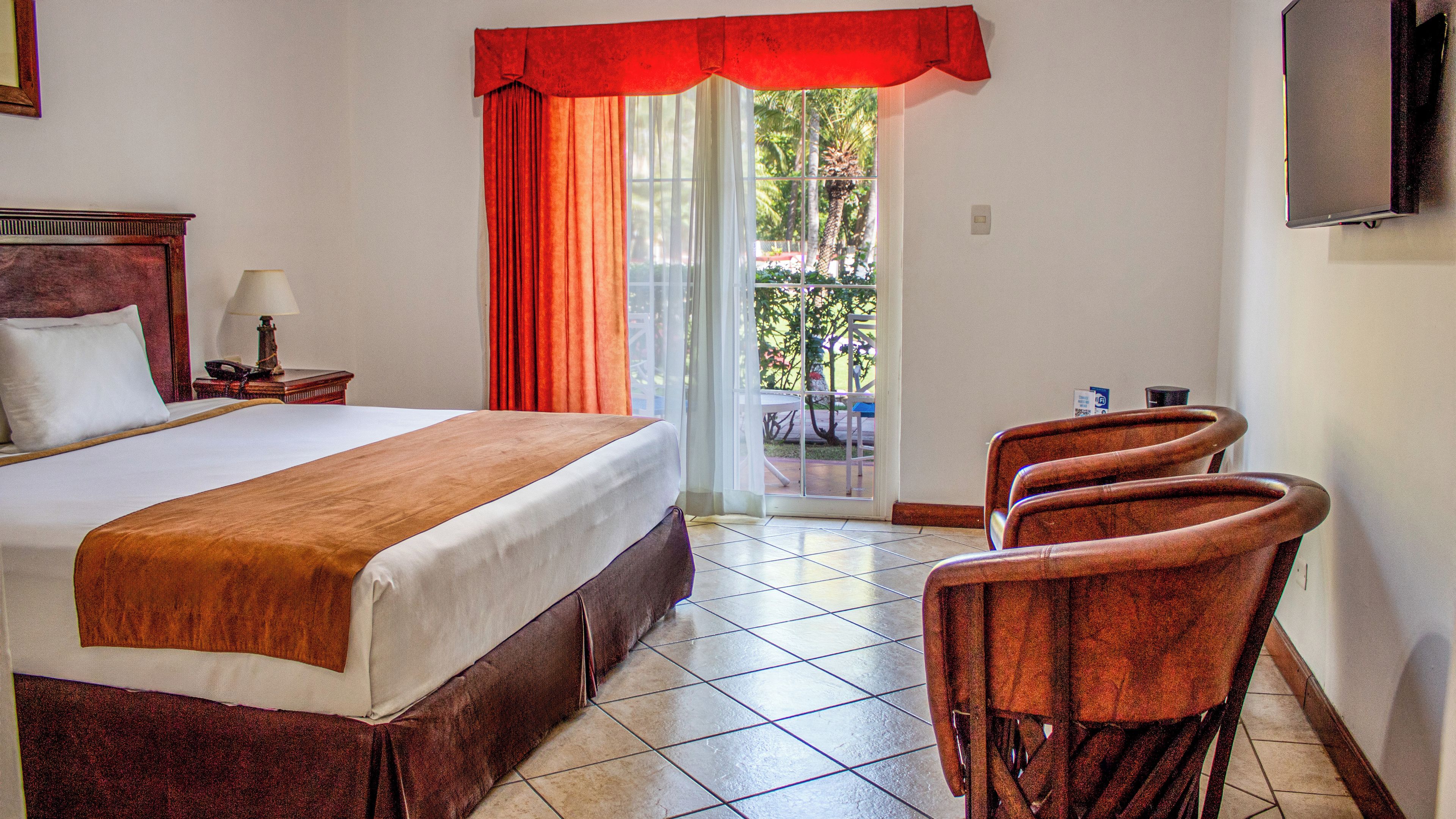 A hotel room with a bed, a desk, a chair, a TV, and a view of the outdoors.