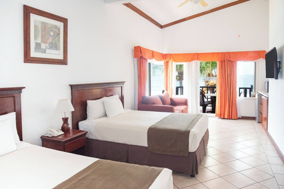 A hotel room with a large bed, a bedside table with a lamp, a TV mounted on the wall, and a view of the outdoors through the window.