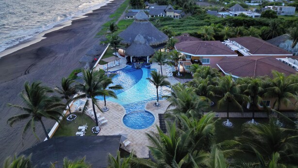 Un resort con piscina, playa y construcciones de techo de paja.