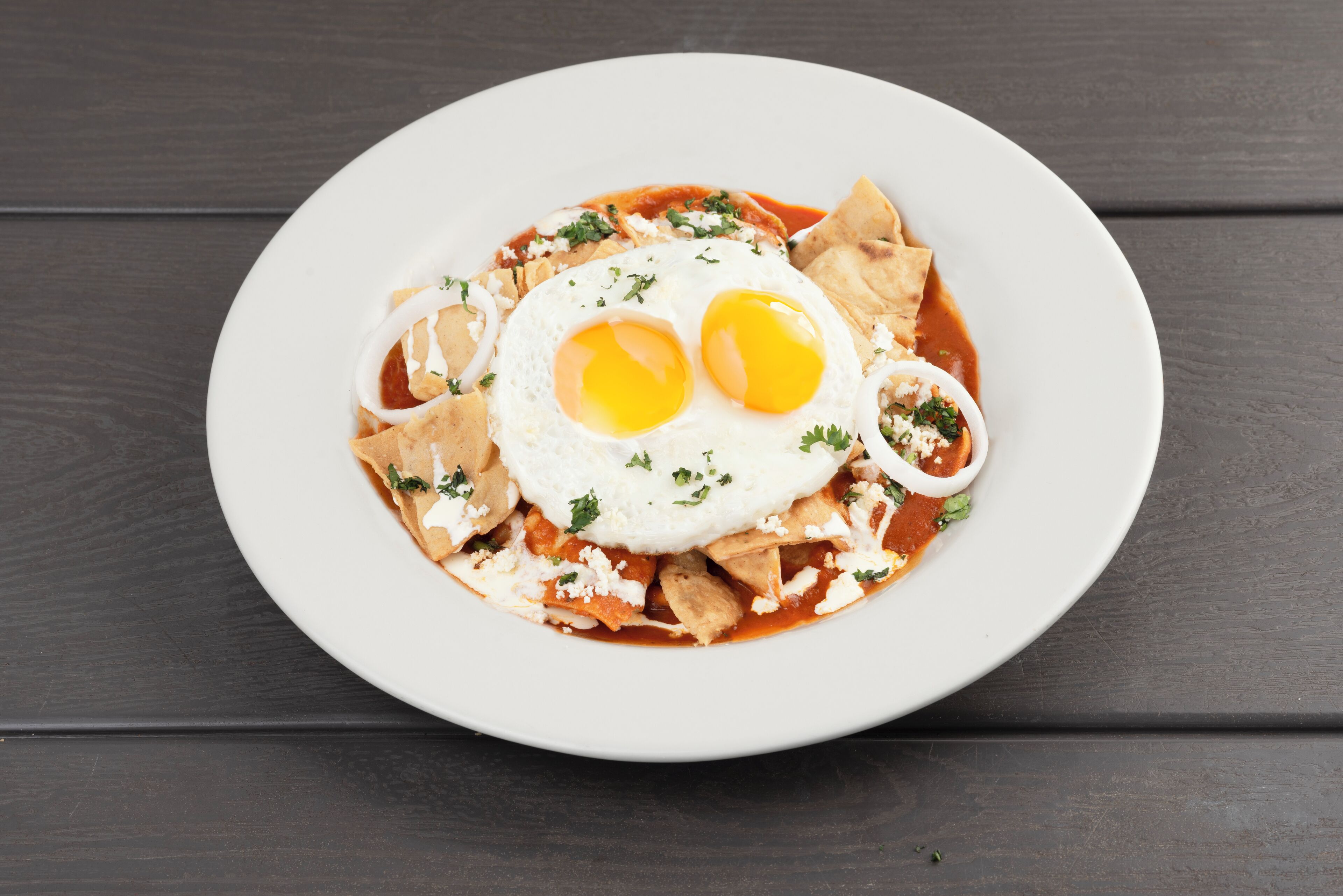 Un piatto di nachos con due uova fritte, formaggio e cipolle su un piatto bianco.