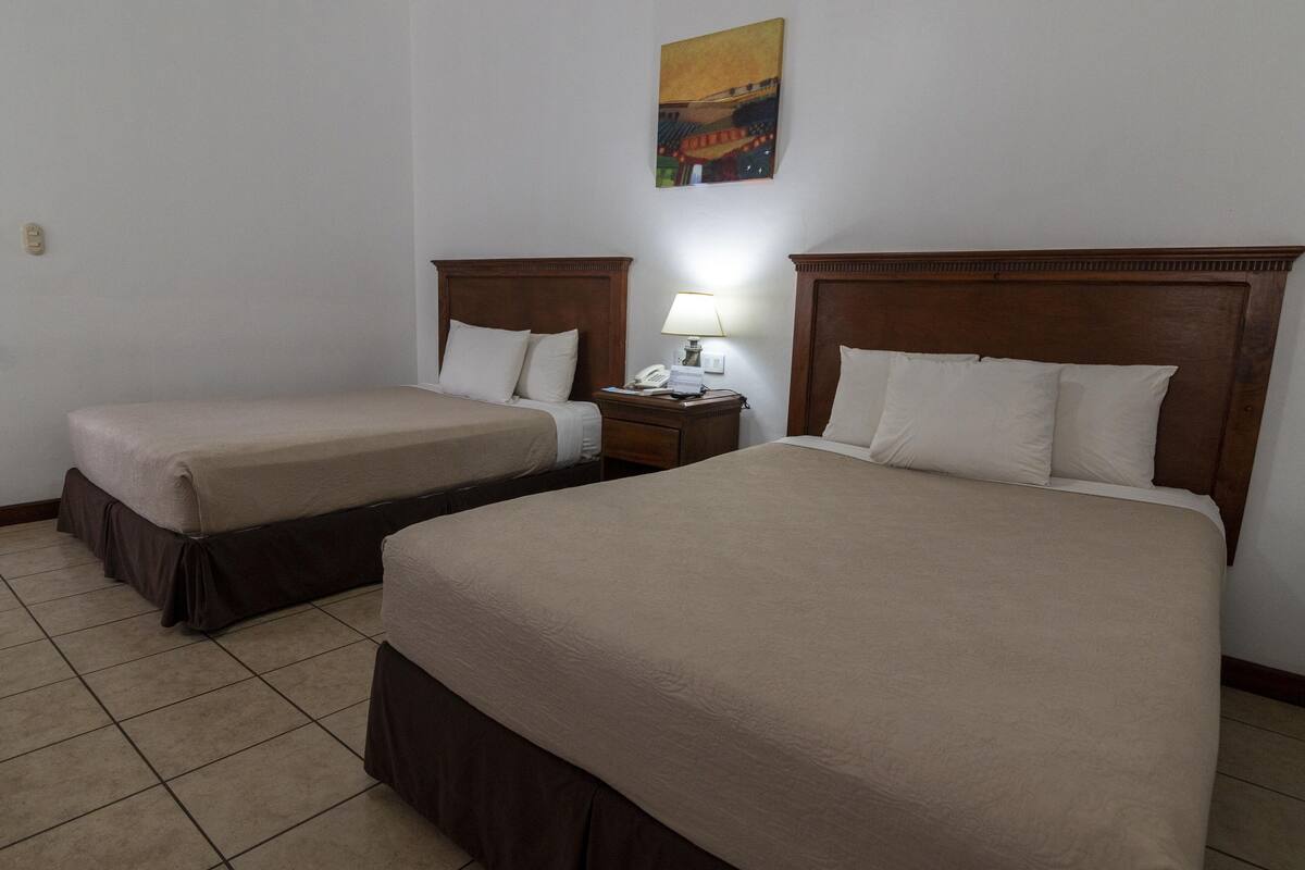 A hotel room with two beds, a nightstand with a lamp, and a painting on the wall.