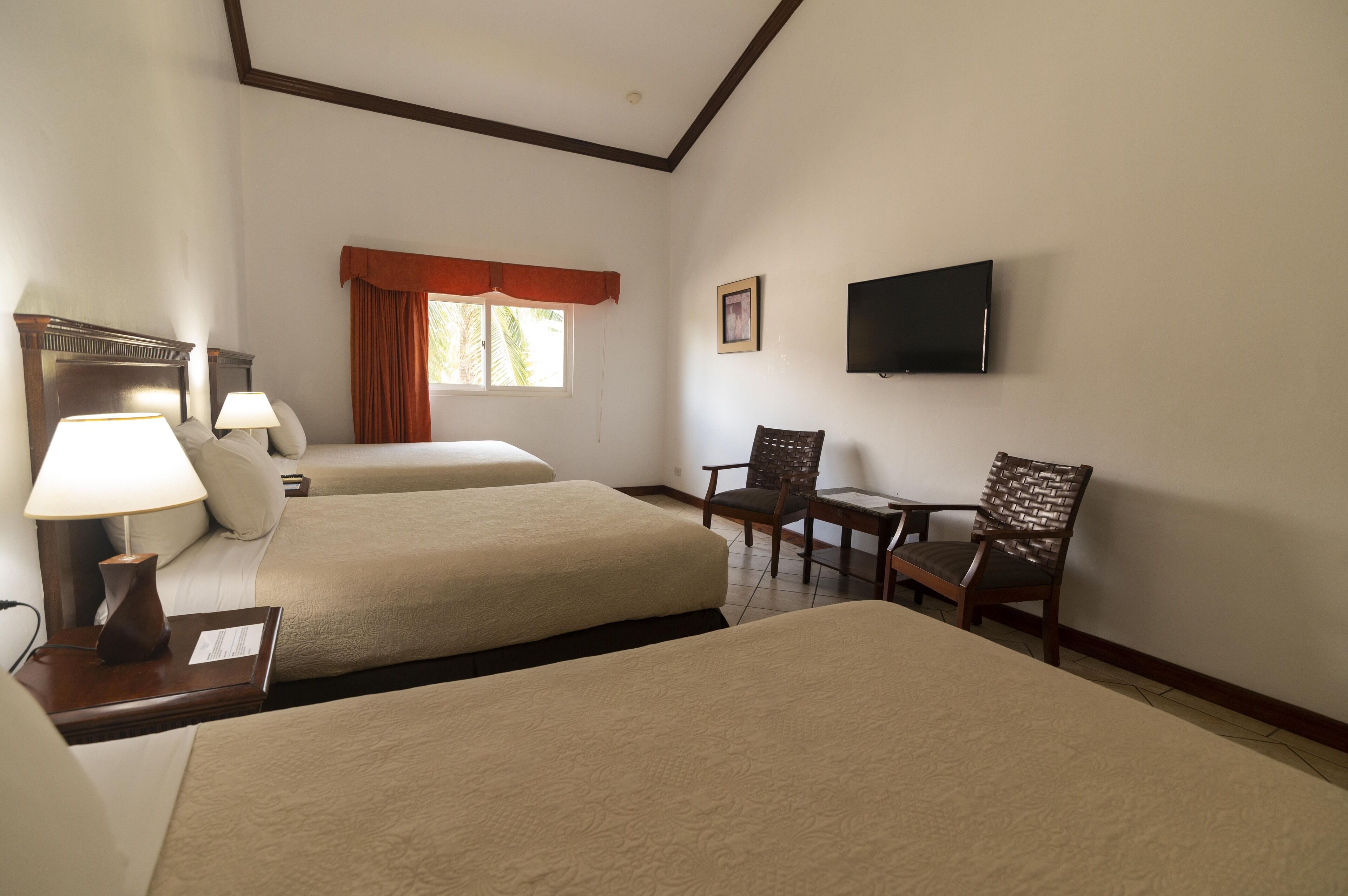 Une chambre d’hôtel avec deux lits, un bureau, une chaise, une télévision et une fenêtre avec des rideaux.