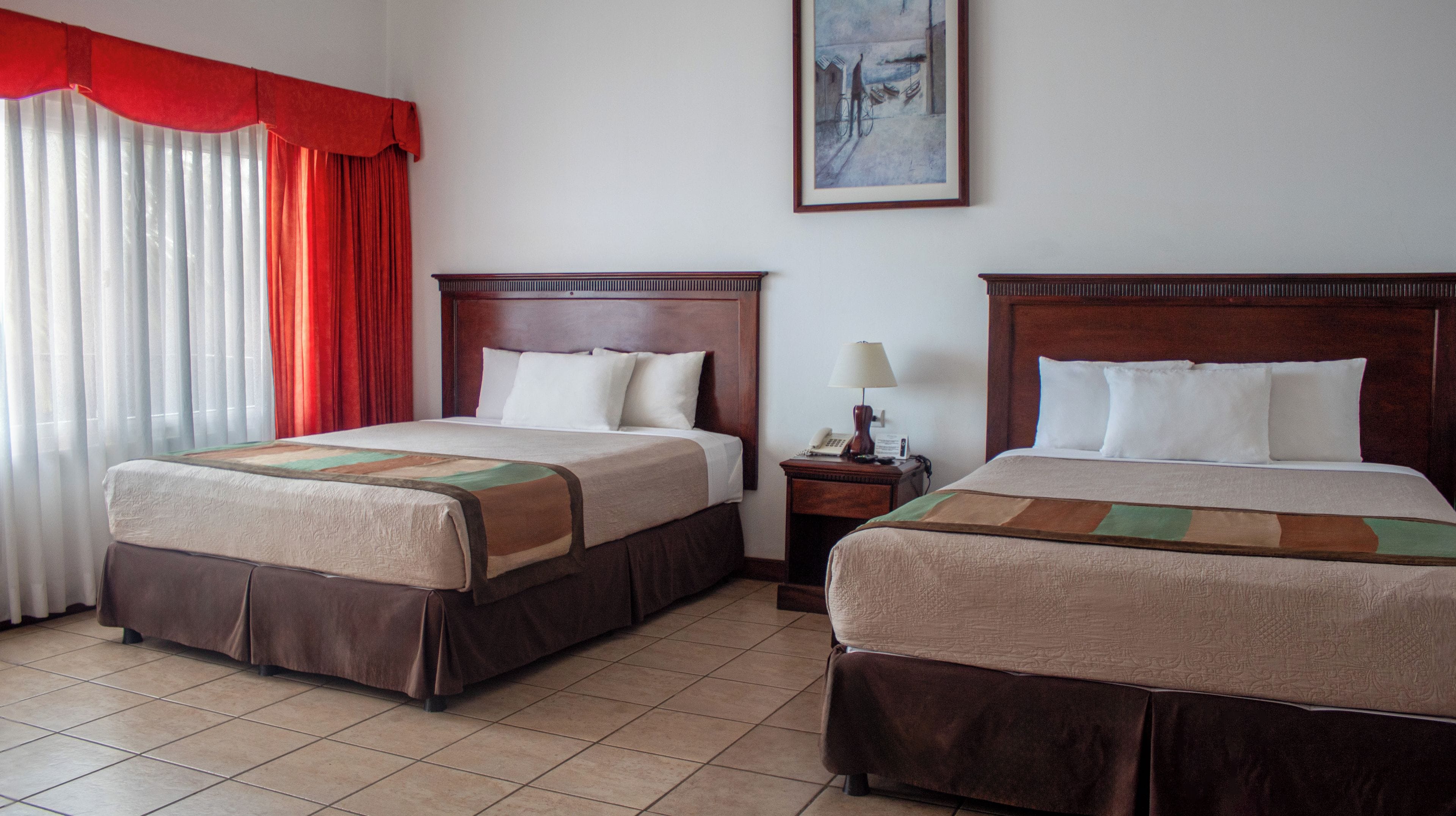 A hotel room with two beds, a nightstand, a lamp, and a painting on the wall.