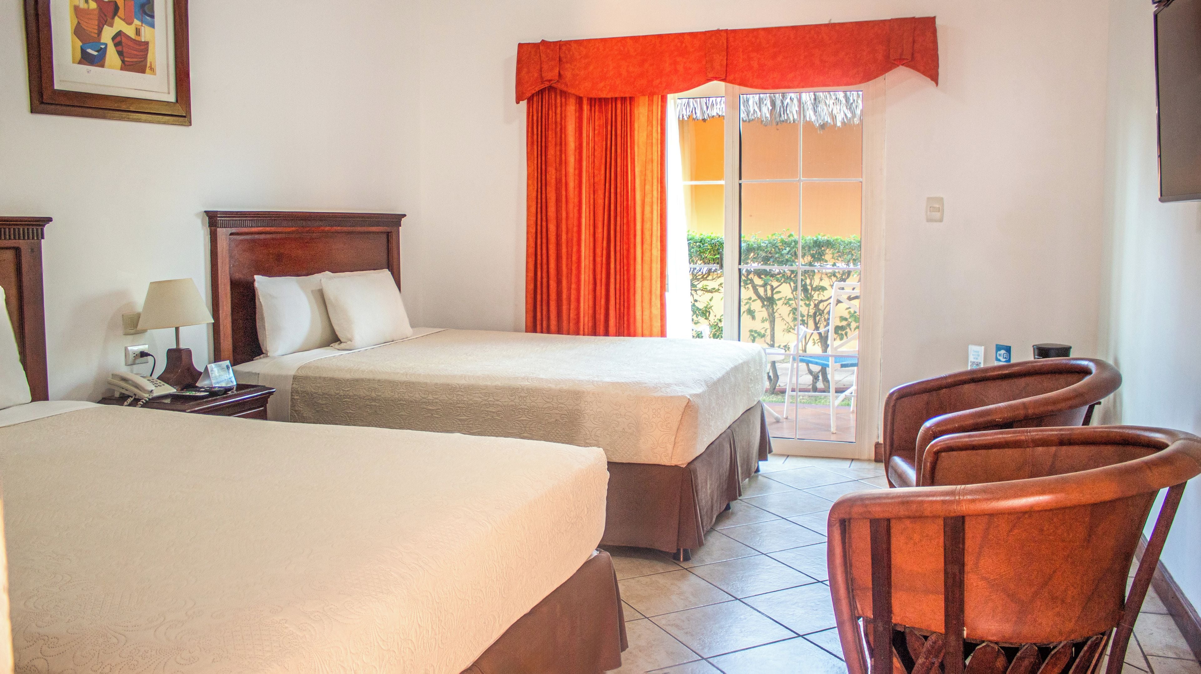 Une chambre d’hôtel avec deux lits, un bureau avec une lampe, une chaise et une vue sur l’extérieur.
