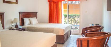 Habitación de hotel con dos camas, un escritorio con lámpara, una silla y vistas al exterior.