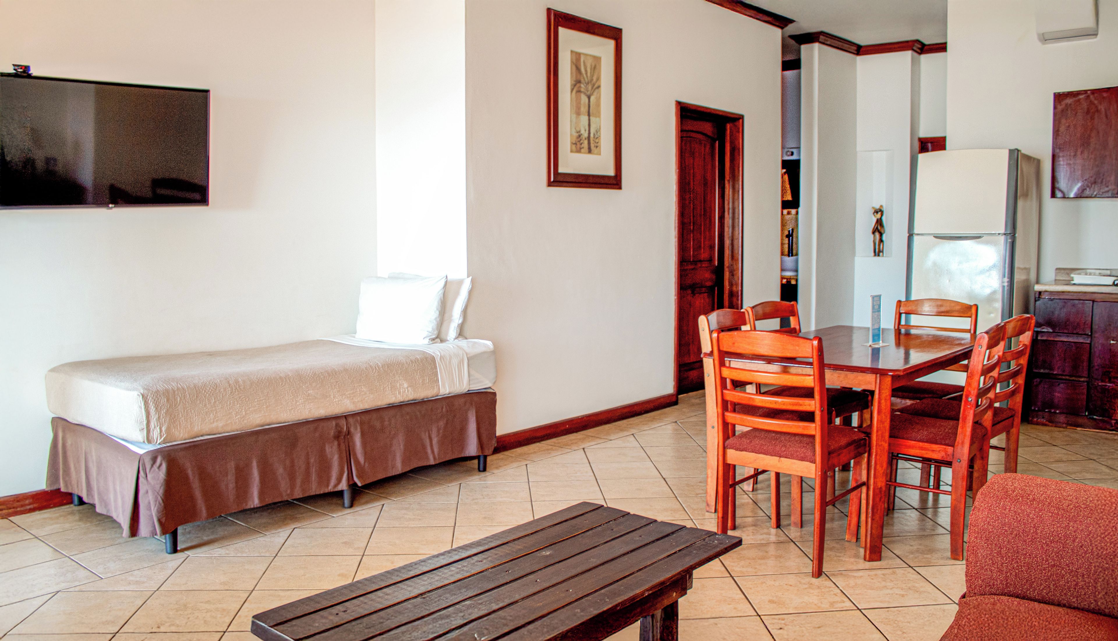Quarto com uma cama, uma mesa de madeira e um espaço de refeições com cadeiras.