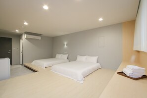 Quarto de hotel moderno com duas camas, uma pequena escrivaninha, ar condicionado fixado na parede e um porta-bandeja com toalhas dobradas.