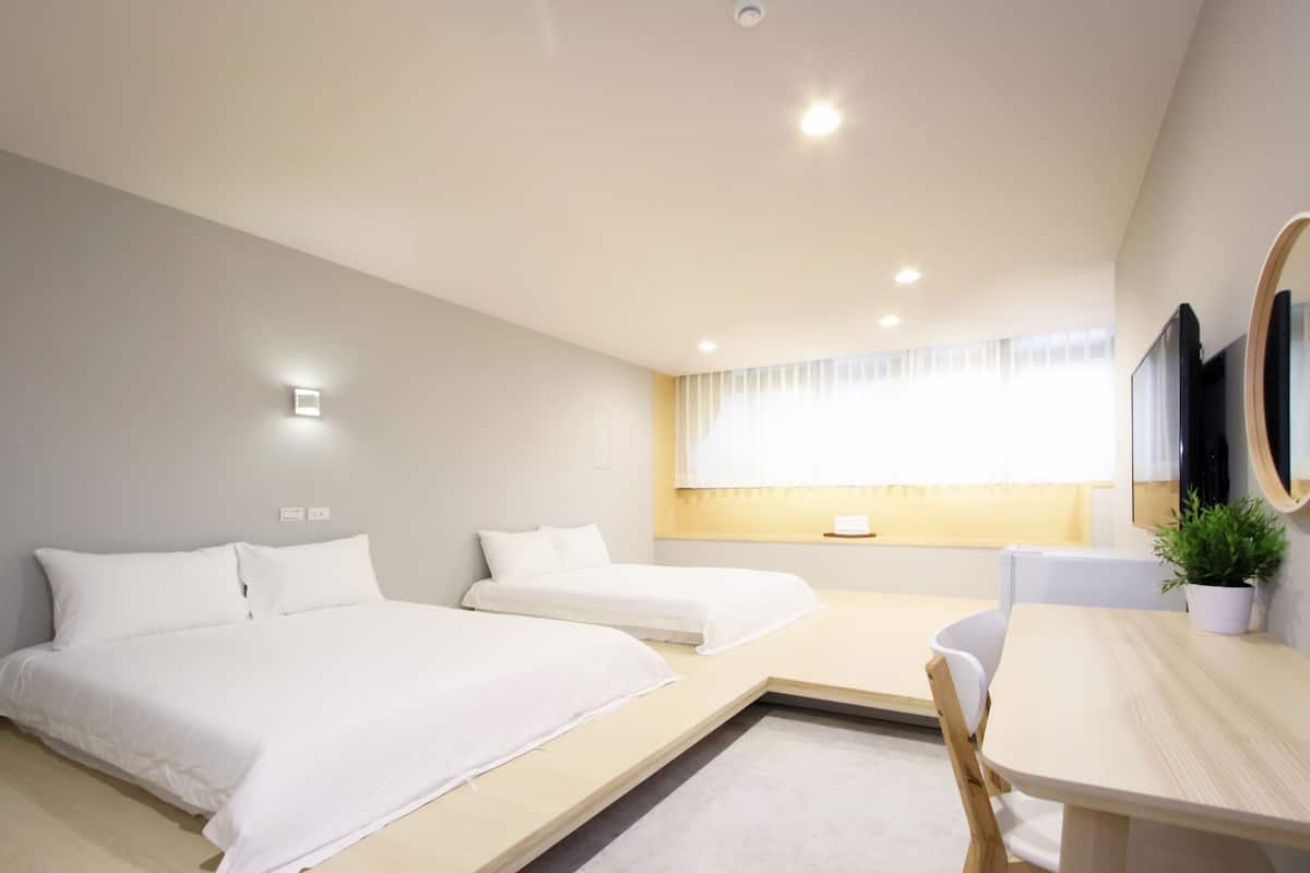 A modern hotel room with two beds, a small table, a chair, a potted plant, and a large mirror.