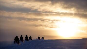 A group of snowmobiles on a snowy landscape during sunset.