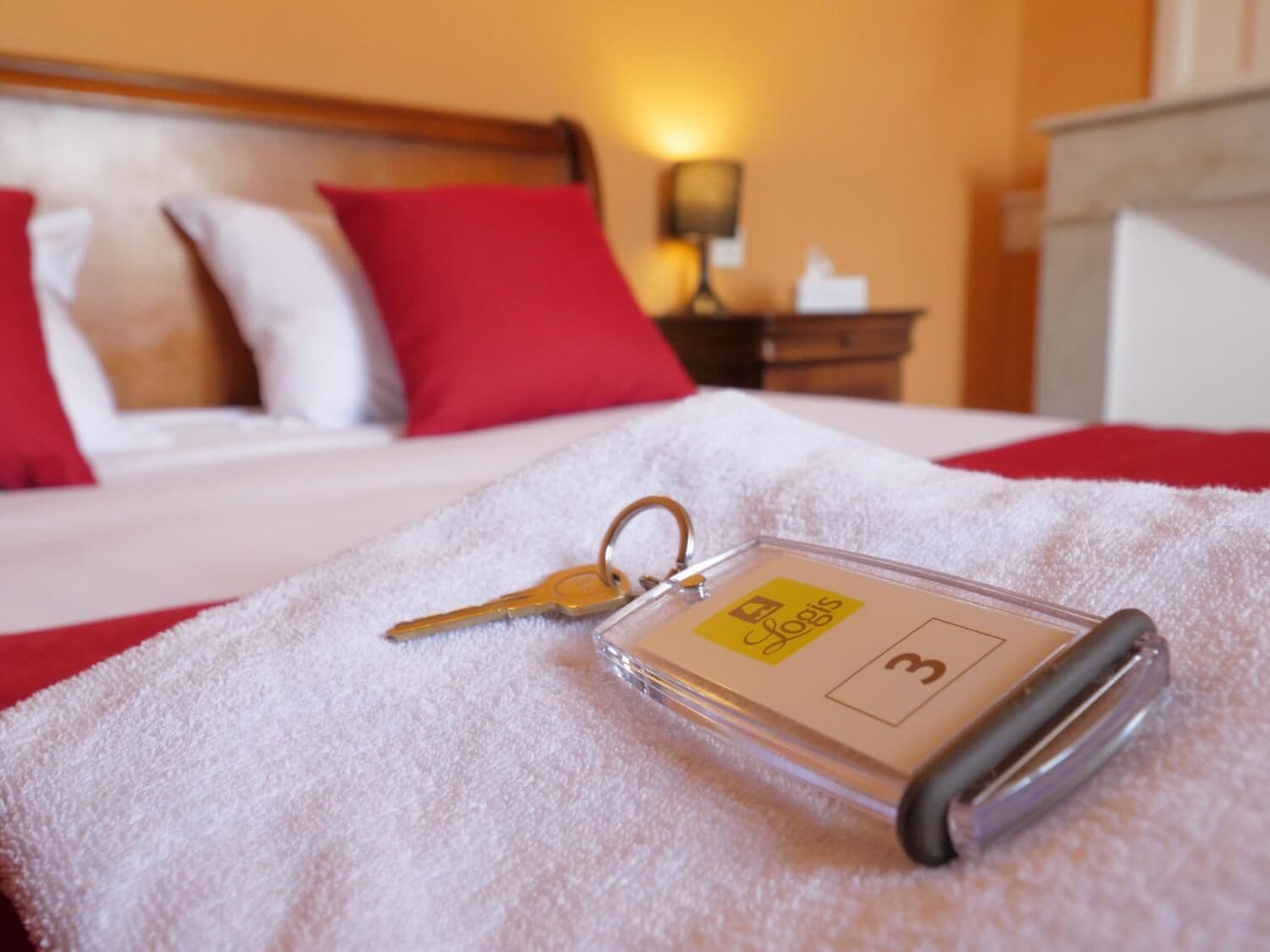 A hotel keychain on a white towel with a bed in the background.