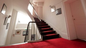 Una escalera con alfombra roja que conduce a una plataforma, paredes blancas y una lámpara moderna.