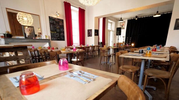 Un restaurante con mesas y sillas de madera, un menú en una pizarra y cortinas rojas.