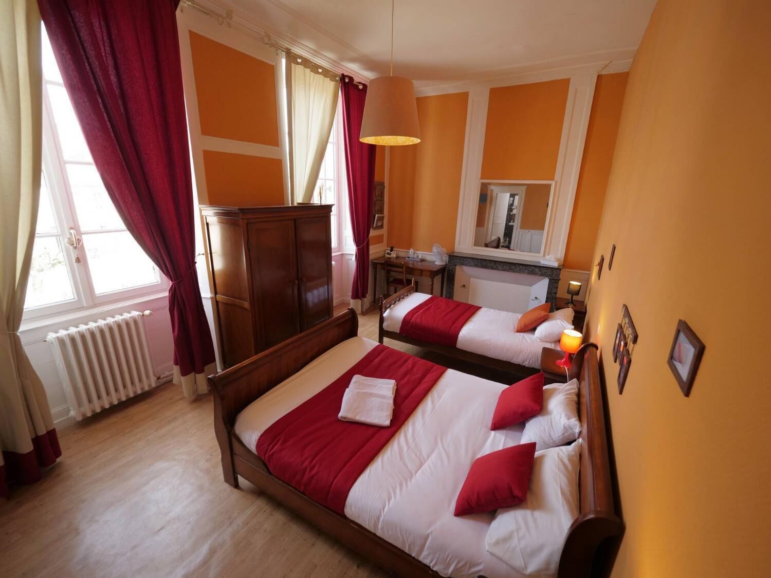 Une chambre d’hôtel avec deux lits, une armoire en bois, un bureau avec une chaise et un miroir au mur.