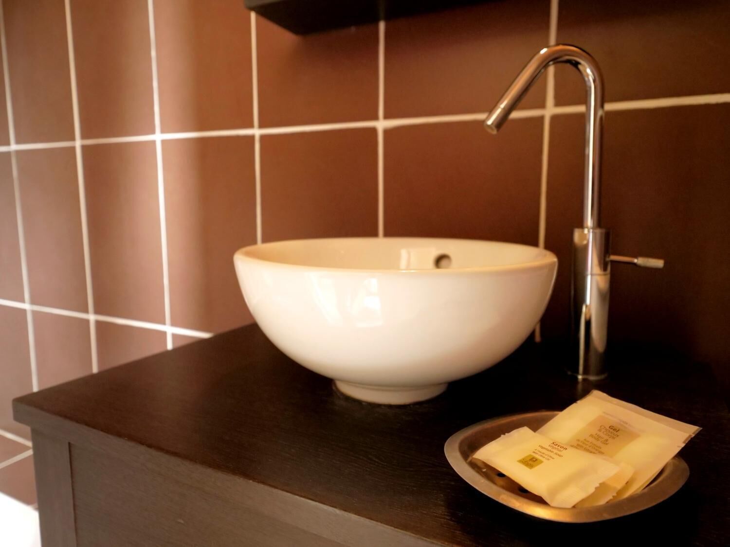 Un lavabo bianco su un piano d'appoggio scuro, con un rubinetto e un vassoio contenente un fazzoletto e una piccola confezione.