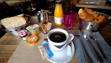 Ein Frühstückstisch mit Brot, Croissants, Kaffee und Beilagen.