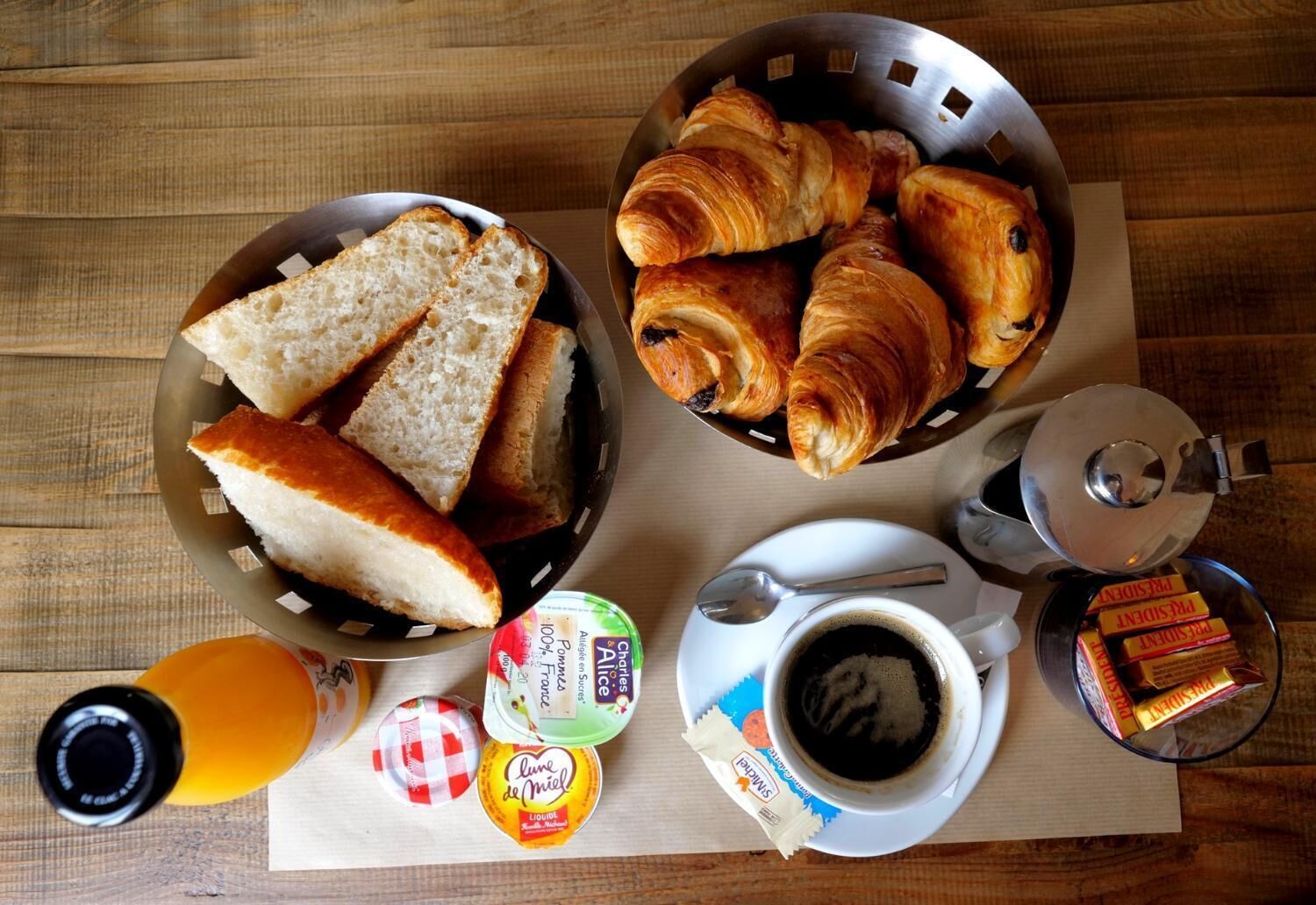 Een ontbijt met brood, croissants, een koffiekopje en toevoegingen op een houten tafel.