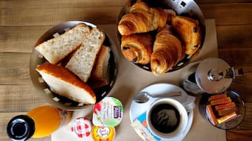 Een ontbijt met brood, croissants, een koffiekopje en toevoegingen op een houten tafel.