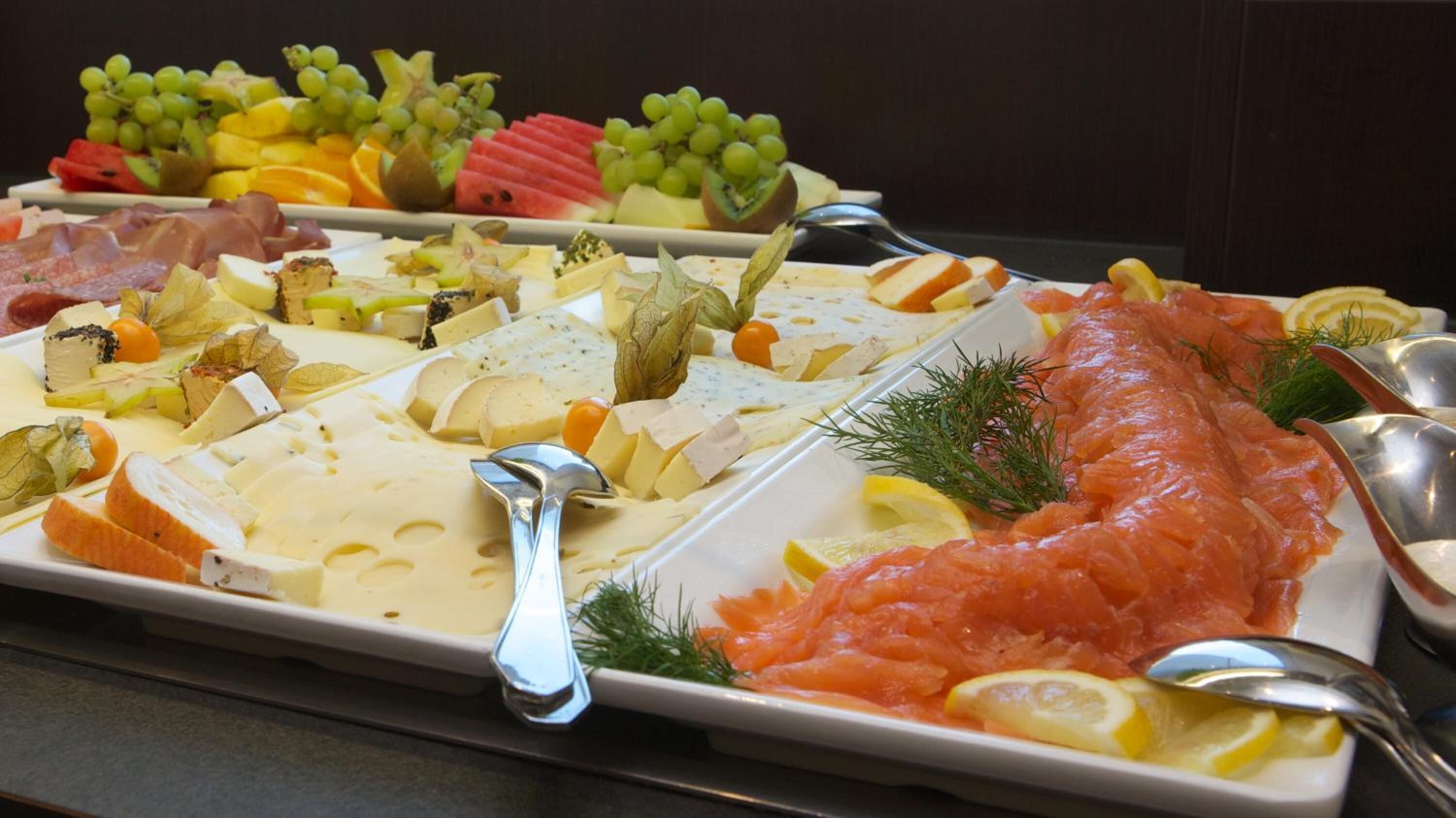 A buffet with various cheeses, fruits, and smoked salmon.
