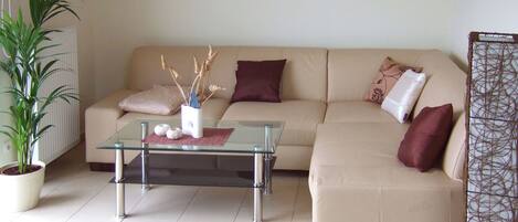 A living room with a beige sofa, a glass coffee table, and a potted plant.