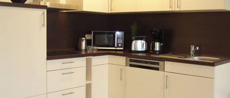 A modern kitchen with white cabinets, a microwave, toaster, coffee maker, and a sink.
