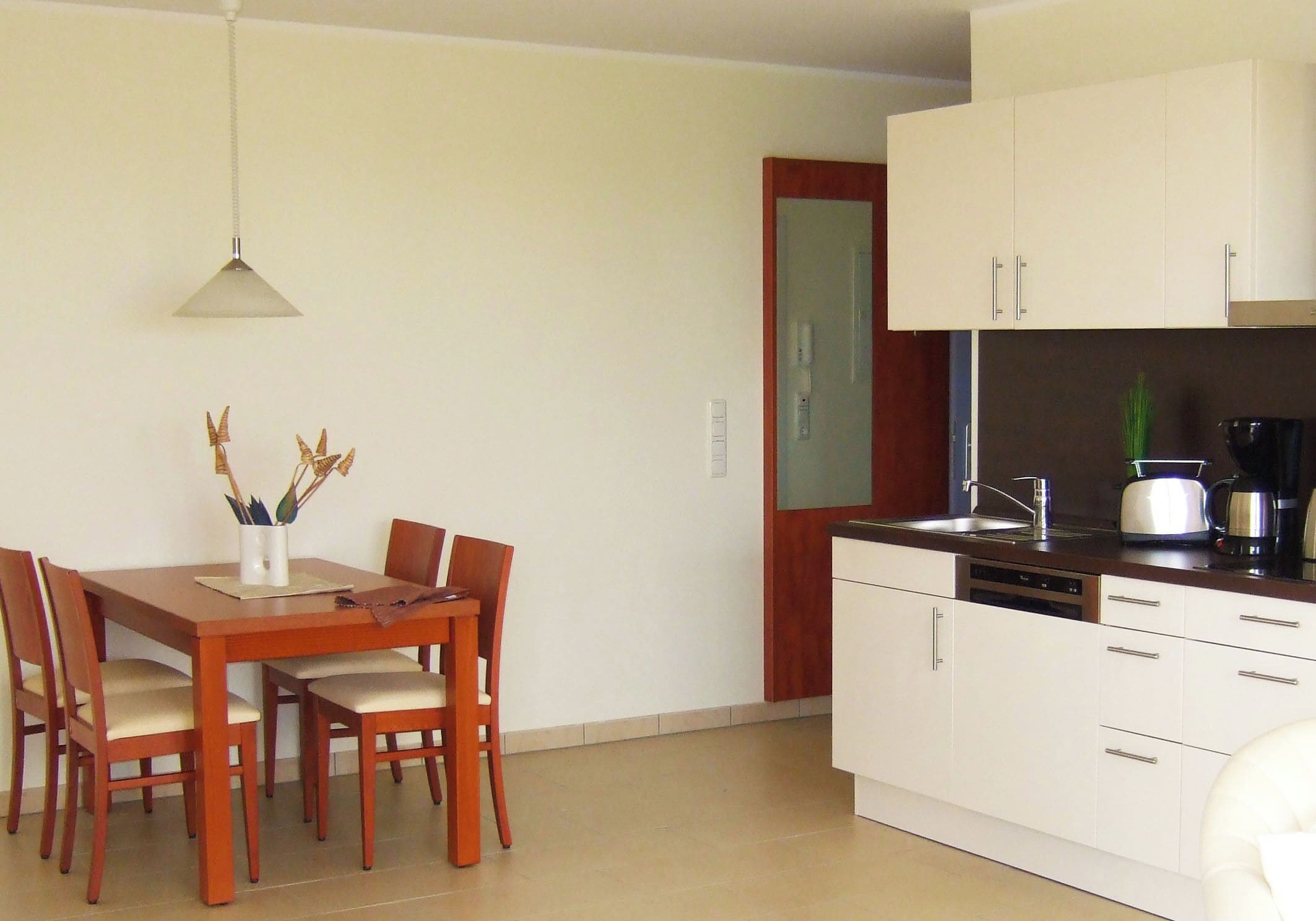A compact kitchen with white cabinets, a dining table with chairs, and a hanging light fixture.