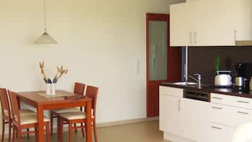 A compact kitchen with white cabinets, a dining table with chairs, and a hanging light fixture.