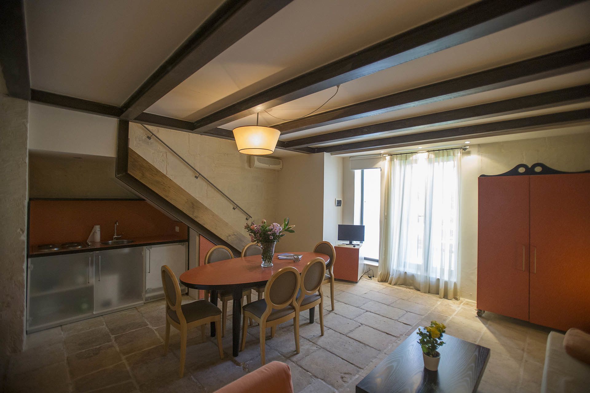 Un área de comedor con una mesa redonda y sillas, una escalera, una cocina y un televisor al fondo.