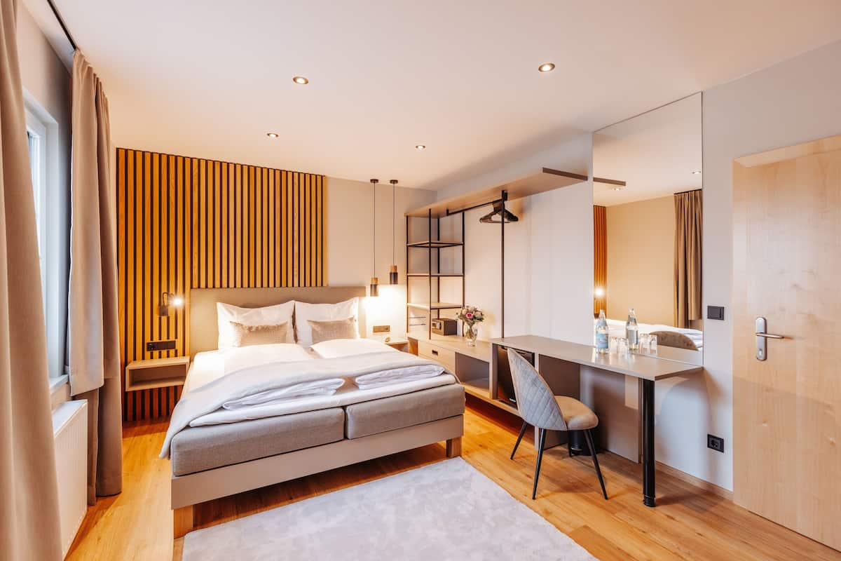 A modern bedroom with a bed, bedside table, desk, chair, and a large mirror.