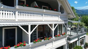 A two-story building with balconies, large windows, and red flowers.