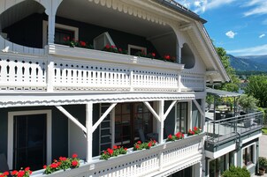 Um edifício de dois andares com varandas, janelas amplas e flores vermelhas.
