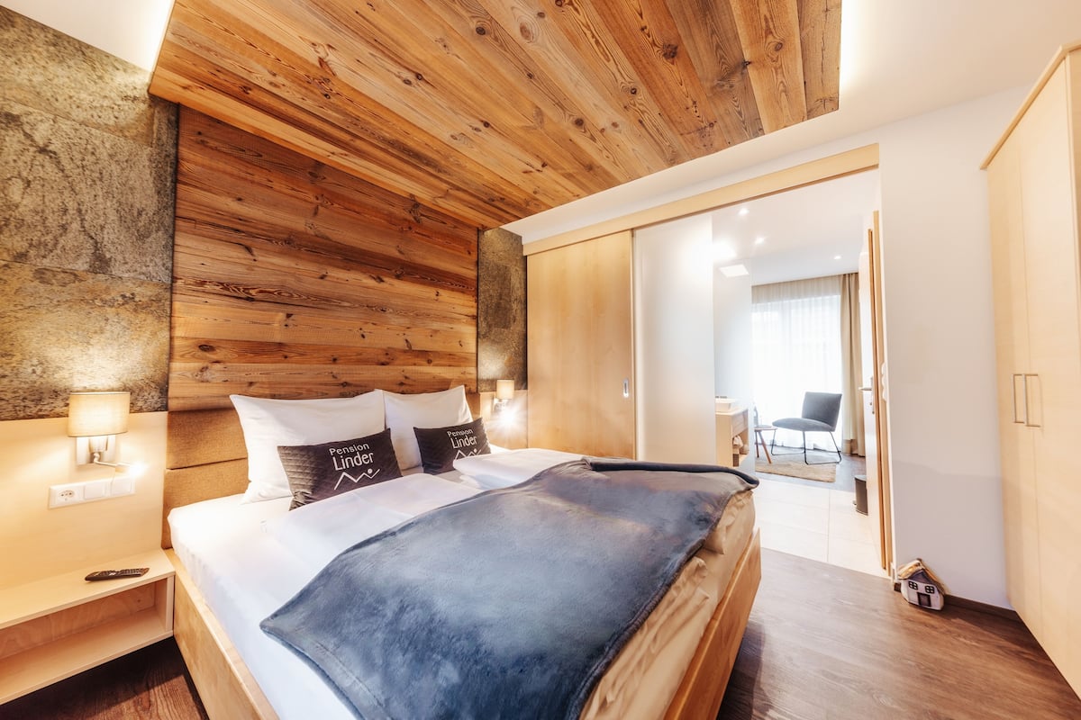 A modern bedroom with a wooden headboard, a large bed, a nightstand, and a bedside lamp.