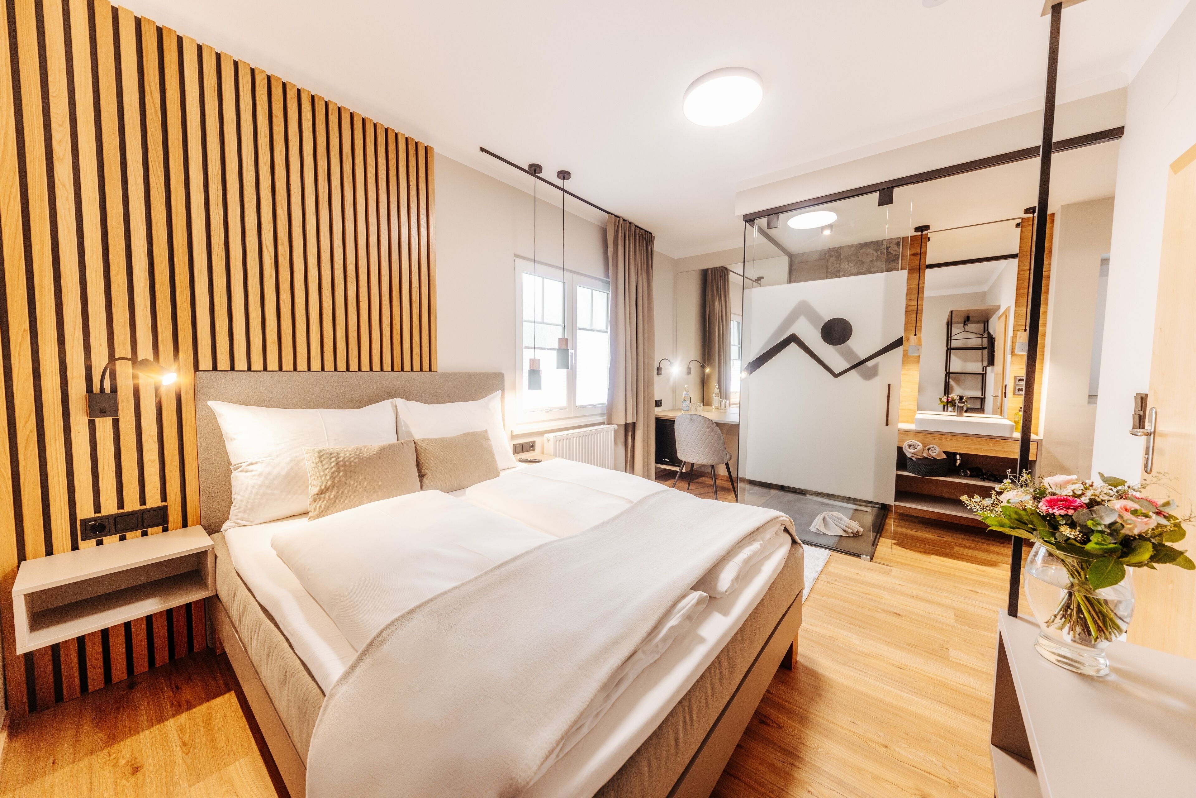 Habitación de hotel moderna con una cama grande, una mesita de noche, un espejo y vistas al baño.