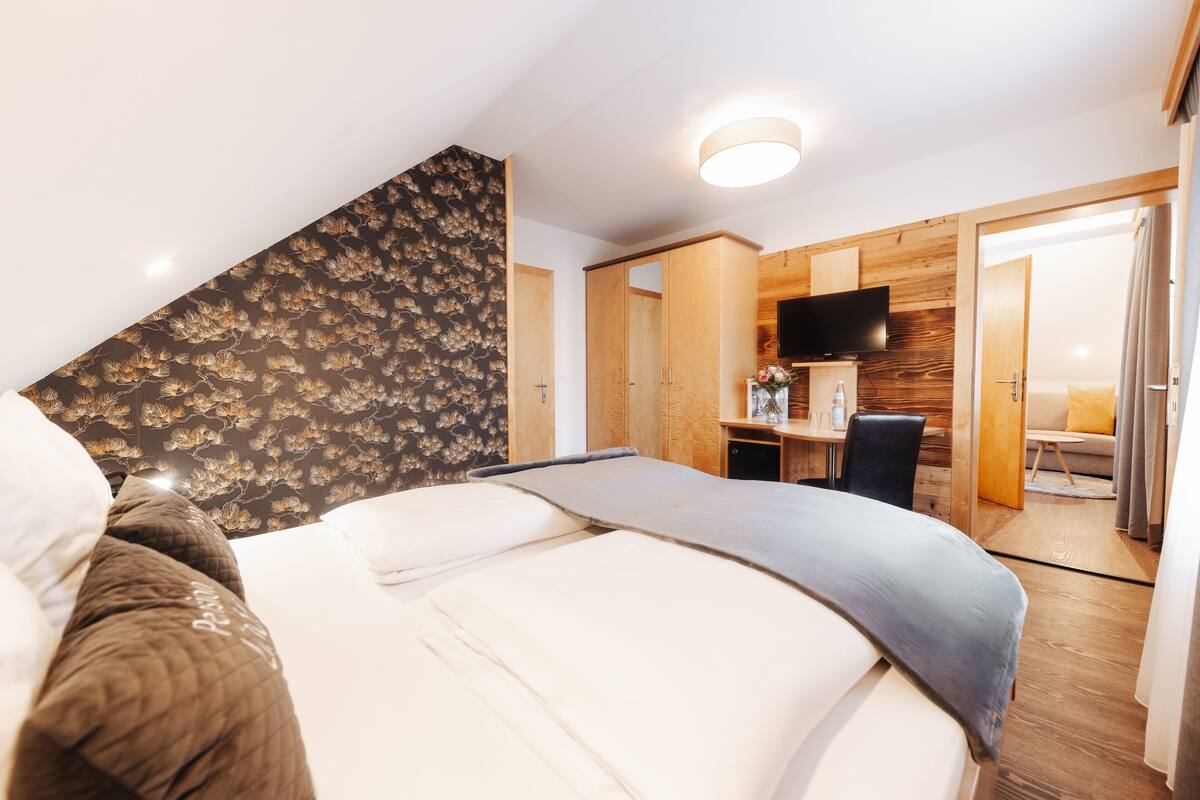 A bedroom with a bed, a desk, a chair, a television, and a bathroom visible through an open door.