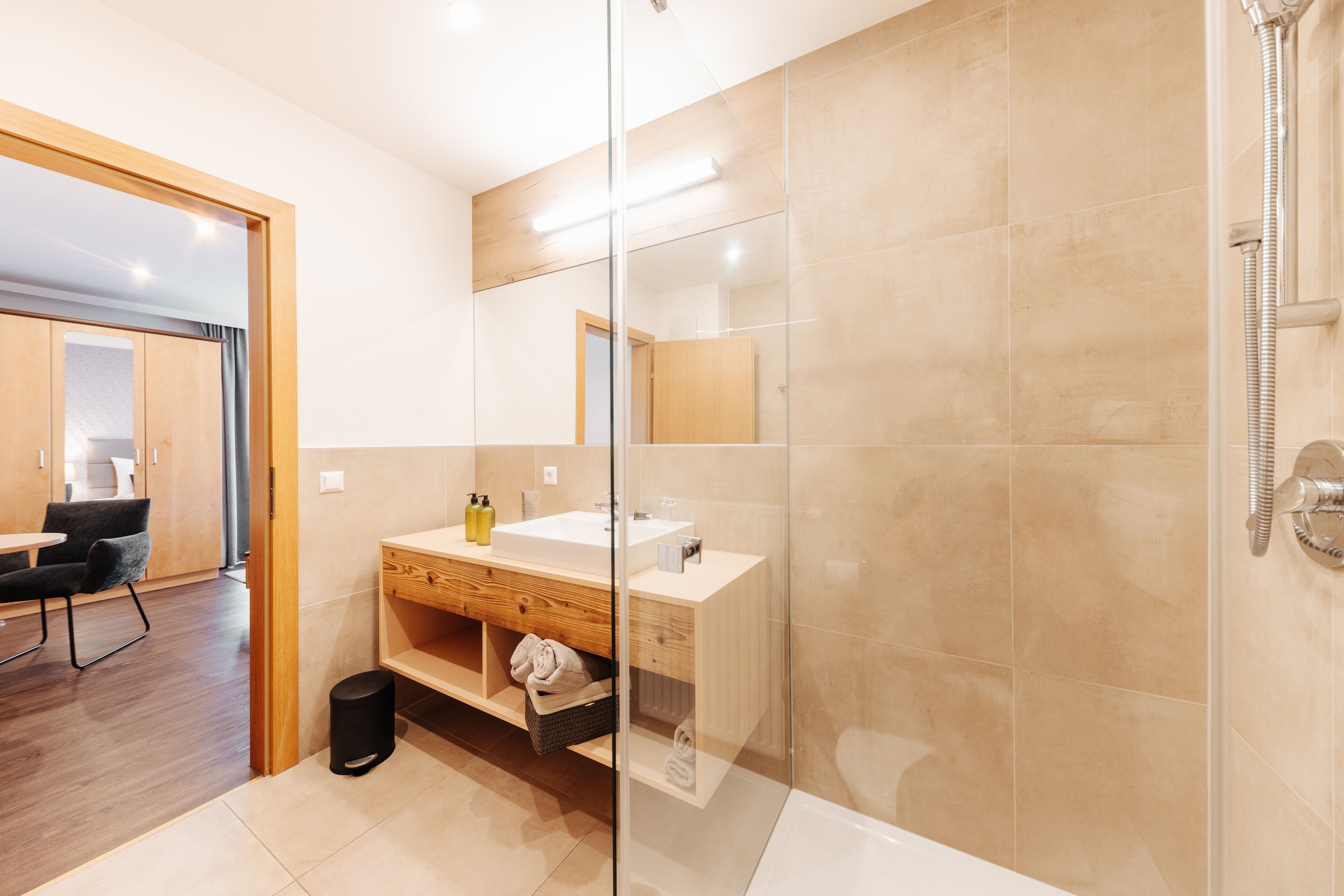 A modern bathroom with a glass shower enclosure, a wooden vanity, and a separate sink area.