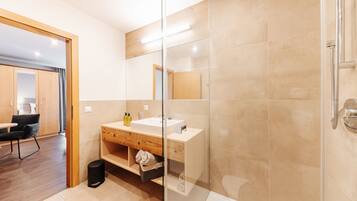 A modern bathroom with a glass shower enclosure, a wooden vanity, and a separate sink area.