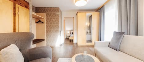 Un salon moderne avec un canapé, un fauteuil et une table basse. On y trouve également une armoire en bois et un mur orné d’un motif.