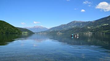 A calm lake with clear water, surrounded by green hills and mountains in the distance.